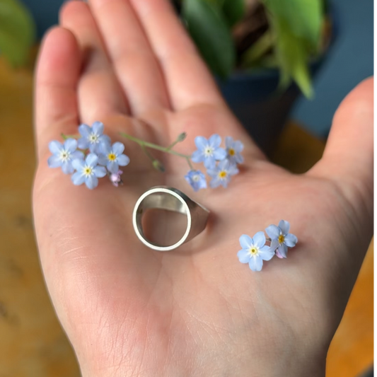 Silver Ring sitting in palm surrounded by blue forget-me-nots flowers
